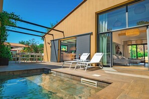 Une maison moderne dotée d’une piscine, d’un espace salon extérieur et de grandes fenêtres.