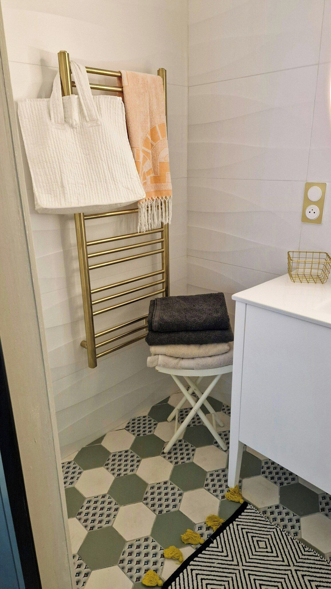 A bathroom with a gold towel rack, a white towel, a patterned towel, a white cabinet, and a hexagonal patterned floor.