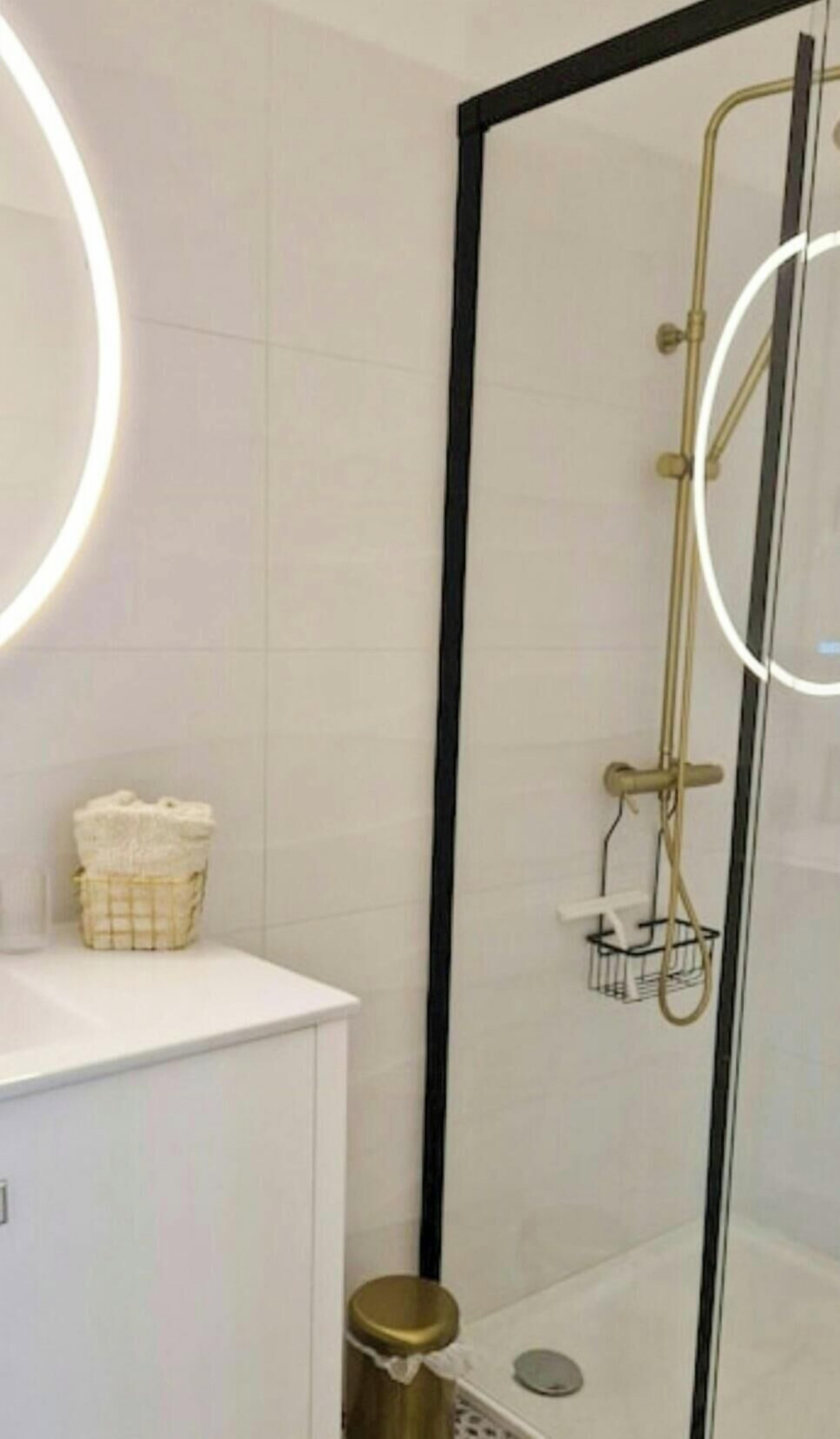 A bathroom with a glass-enclosed shower, a white sink, and a mirror with a circular light.