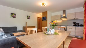 Eine moderne Küche mit Holzausbau, einem Esstisch mit Stühlen, einer Couch und einem an der Wand befestigten Fernseher.