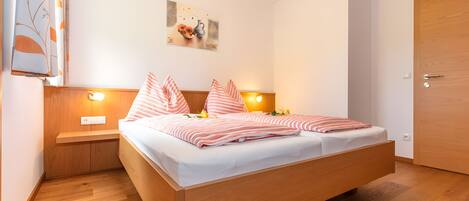 A bedroom with a wooden bed, bedside tables with lamps, a painting on the wall, and a wooden door.