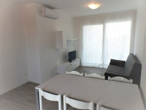 Ein kleiner, moderner Raum mit Esstisch, Sofa, Fernseher und Klimaanlage.