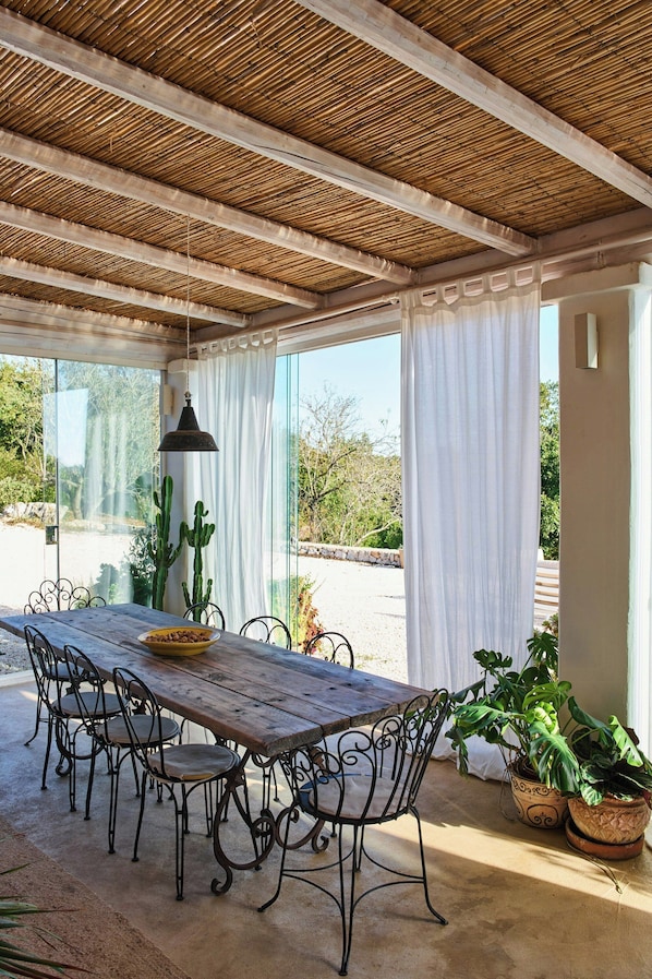 Eine Terrasse im Freien mit einem Holztisch und -stühlen, einer hängenden Leuchte und Blumentöpfen.