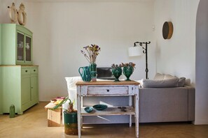Ein Zimmer mit einem grünen Schrank, einem Holztisch mit einer Vase, einem grauen Sofa und einer Wandlampe.