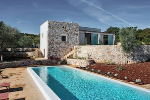Ein modernes Haus mit Natursteinfassade, Swimmingpool und Garten.