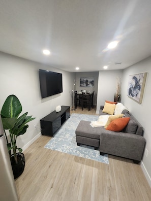 A modern living room with a flat-screen TV, grey sofa, and a dining area with a table and chairs. - Modern and Cozy 2 bedroom Basement Suite with fully equipped kitchen (Calgary)