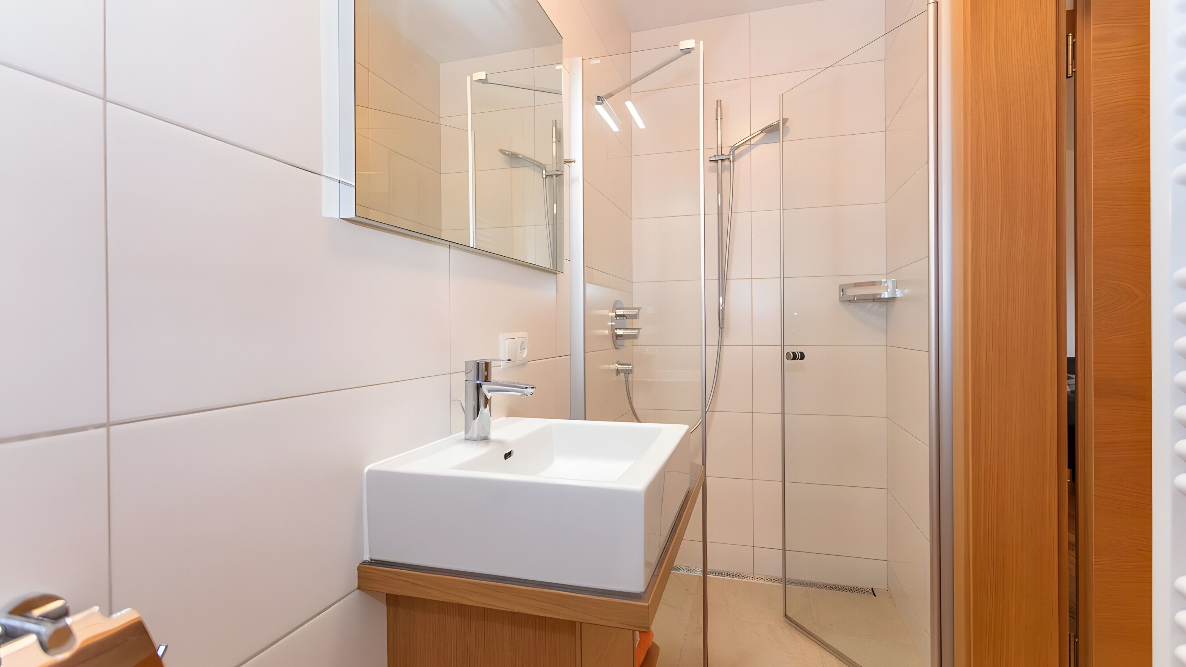 Une salle de bain moderne avec un lavabo blanc, une douche en verre et un meuble-lavabo en bois.