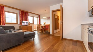 A modern kitchen with wooden cabinets and a built-in oven, a dining area with a table and chairs, and a living room with a sofa and a TV. - Apartment "Panorama" with Mountain Views, Shared Garden, and Wi-Fi (Mittersill)