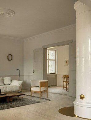 Habitación minimalista con un sofá blanco, una silla de madera, un gran pilar blanco y vistas a través de una puerta abierta.