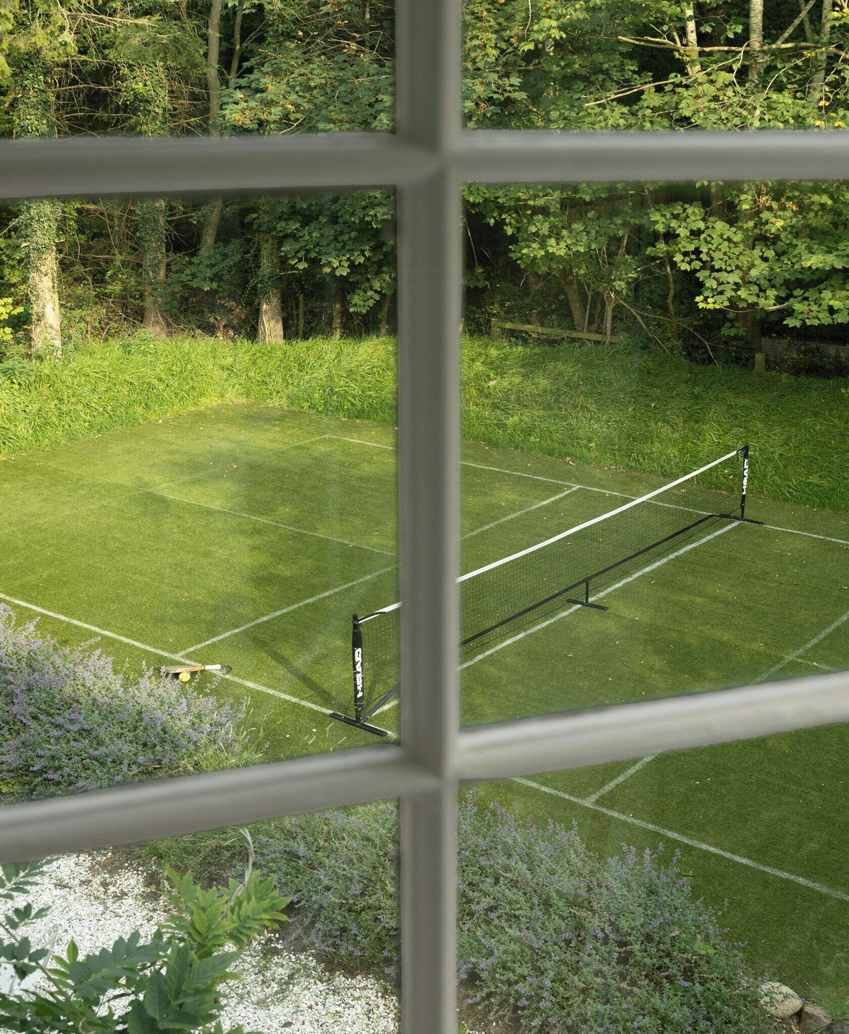 A tennis court with a net, surrounded by greenery and trees.