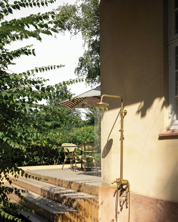A wooden deck with outdoor furniture, a wall-mounted shower, and surrounding greenery.