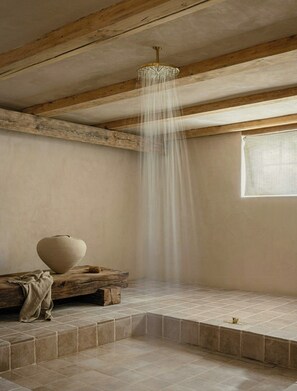 A room with a wooden ceiling, a hanging light fixture, a large vase, and a window.