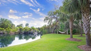 Un área verde bien cuidada con un estanque, árboles y una hamaca.