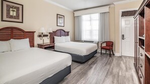 Una habitación de hotel con dos camas, un escritorio, una silla, un armario y un ventilador de techo.