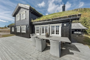 Ein Holzhaus mit Terrasse, Fenstern mit weißen Rahmen und einem grasbewachsenen Dach.