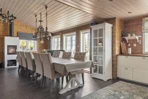 Ein Holzinterieur mit einem Esstisch, Stühlen, einer Chandelüster, einem Kamin und einem Schrank.