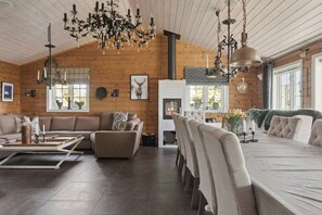 Ein geräumiger Raum mit Kamin, Holzwänden, einer Chandelier und einem Essbereich.