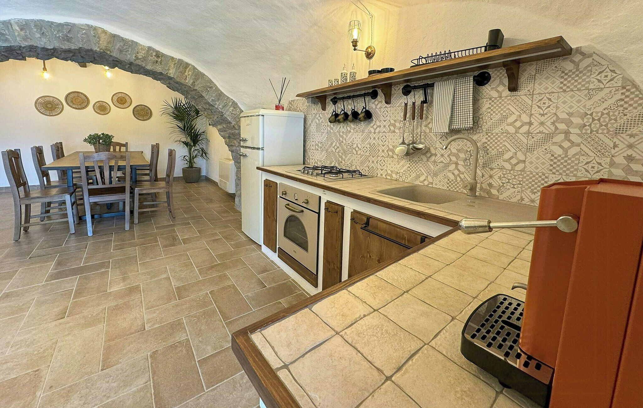 Une cuisine avec une arche en pierre, un coin repas avec des meubles en bois et un mur de crédence orné de motifs.