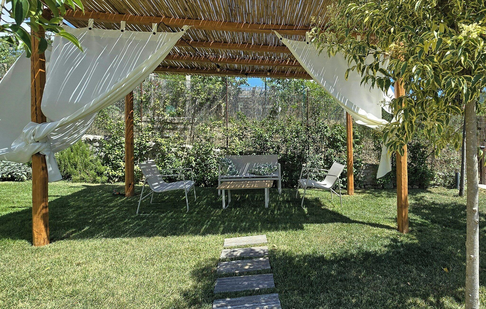 Ein überdachter Außenbereich mit einer Pergola, zwei Stühlen und einem Tisch.