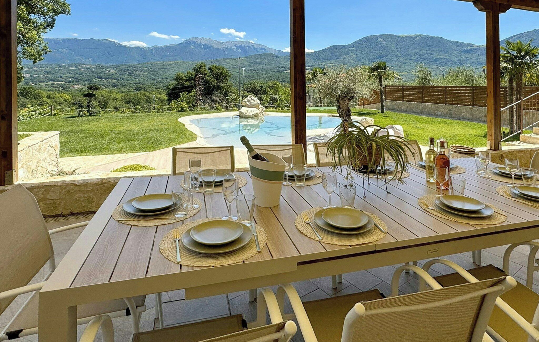Un espacio exterior para comer con una mesa lista para cuatro personas, con vistas a un paisaje montañoso y un jacuzzi.
