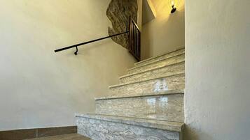 A staircase with stone steps and a handrail, a wall with a textured pattern, and a light fixture.