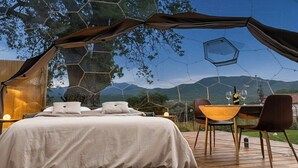 Un dormitorio con cama, almohadas, una mesa con vasos y una botella, y vistas a las montañas.
