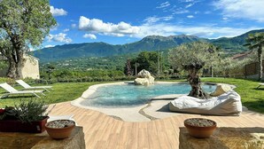 Piscina con vista a la montaña, sillas de descanso y una mesa de piedra con cuencos.