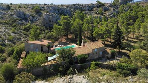 Una casa de pedra amb piscina, envoltada d'arbres i un paisatge rocos.