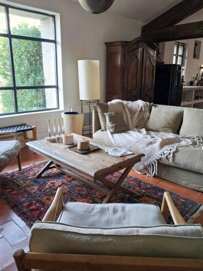 Ein gemütliches Wohnzimmer mit einer Couch, einem Couchtisch, einer Lampe und einem Fenster mit Blick auf Grün.