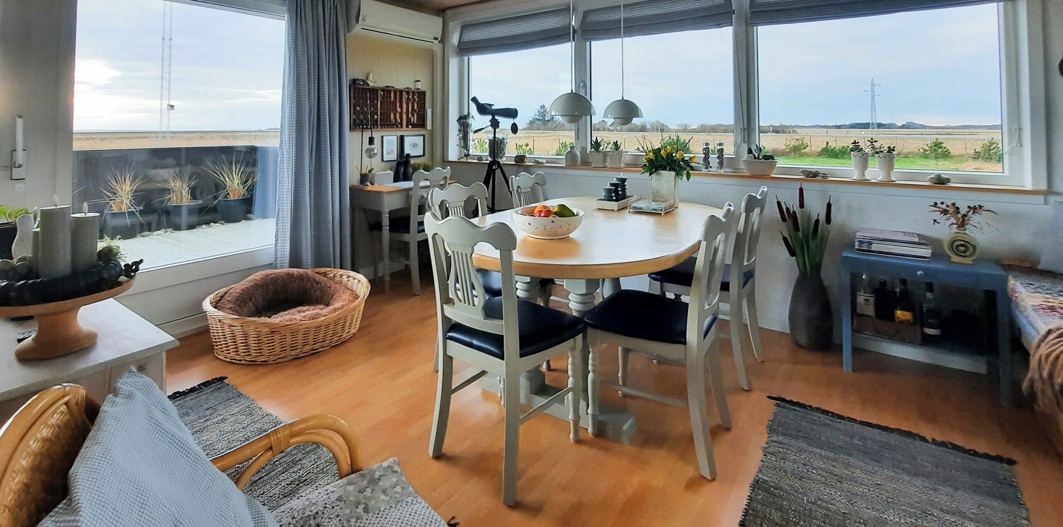 A dining area with a round table, white chairs, and a view of the countryside through large windows.