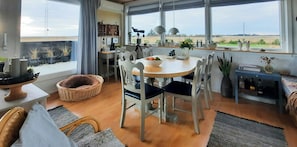 A dining area with a round table, white chairs, and a view of the countryside through large windows. - Holiday home with view over Limfjord (Thyholm)