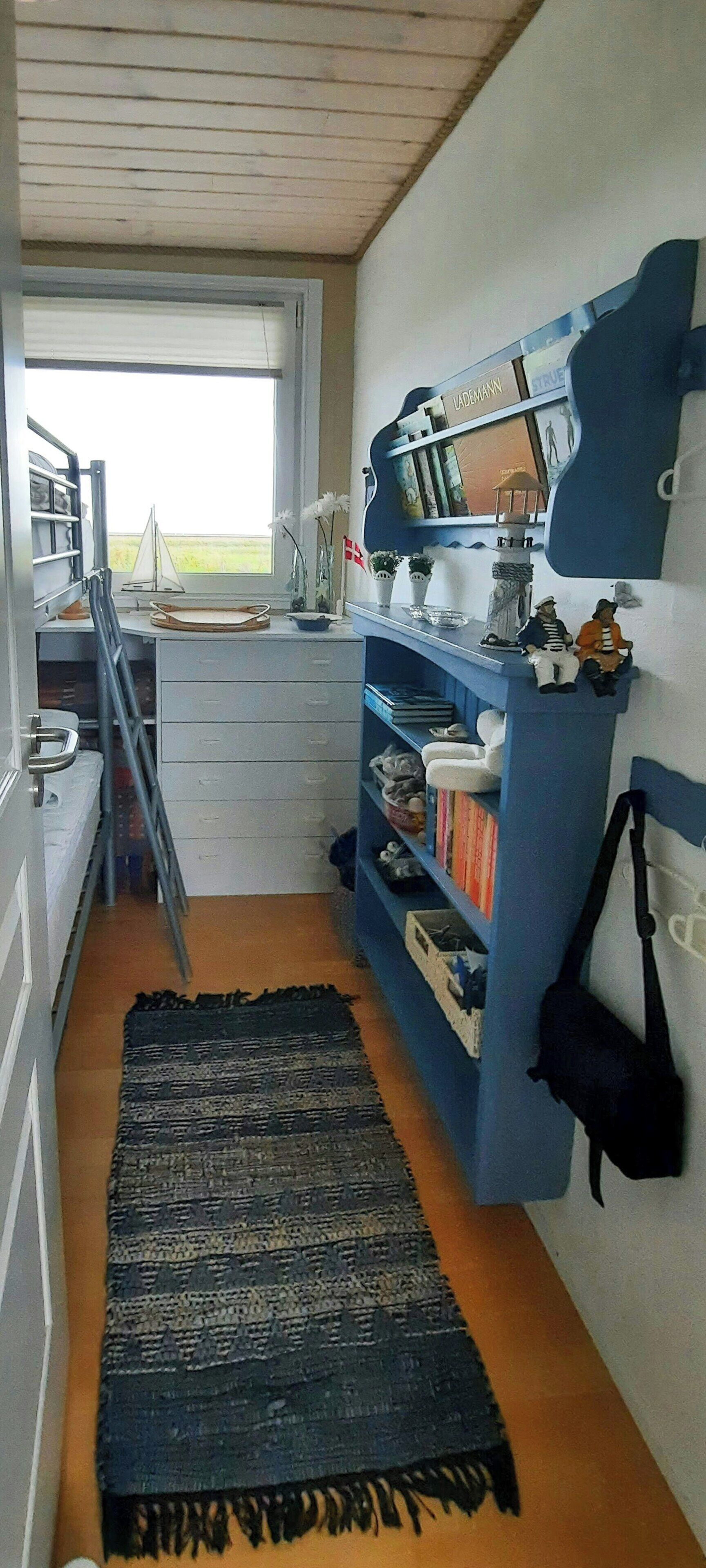 Una habitació estreta amb una finestra, escriptori, prestatgeries i una maqueta d'un veler.
