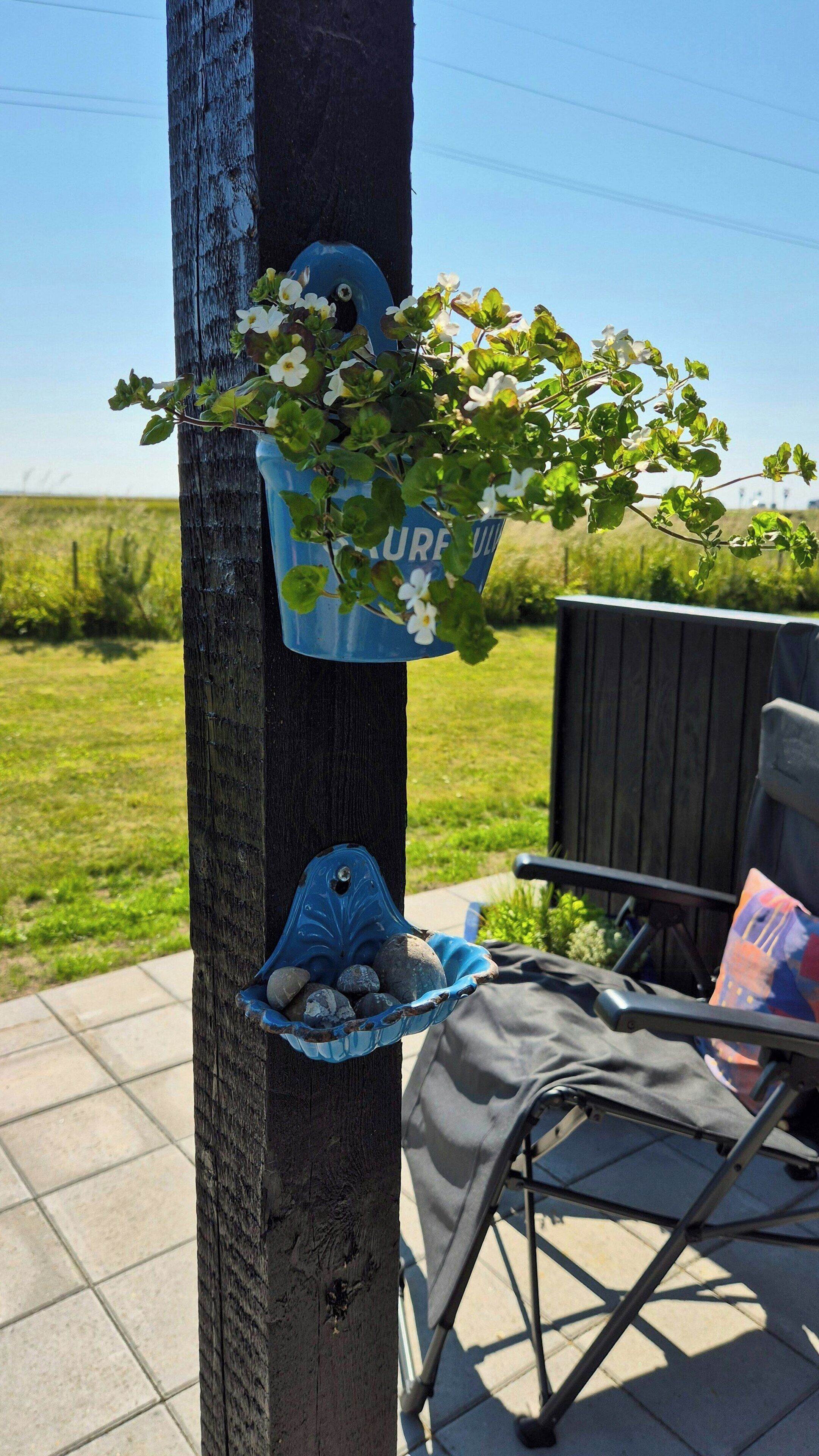 A wooden post with a blue flower pot and a blue bird bath attached to it.