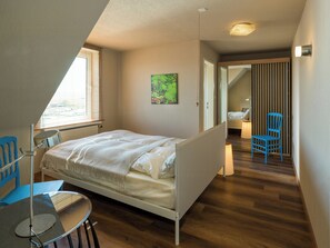 Ein Schlafzimmer mit Bett, Stuhl, Tisch und einem Bild an der Wand.