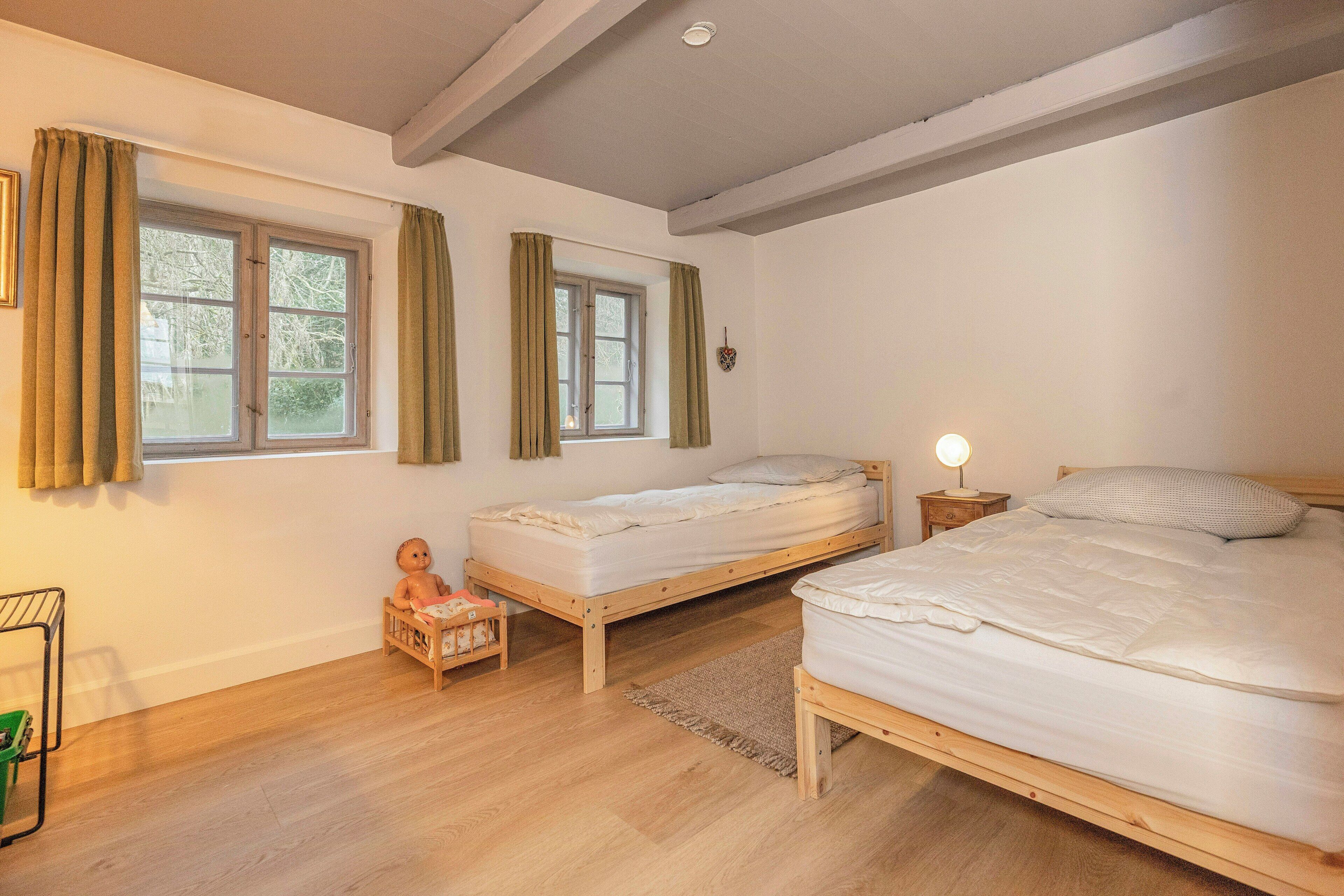 Ein Schlafzimmer mit zwei Betten, einem Fenster, einem Nachttisch und einem Babybett.