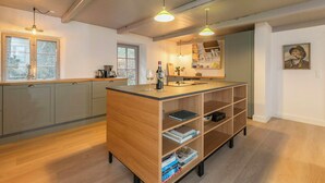 A modern kitchen with grey cabinets, a wooden island with bookshelves, pendant lights, and a view of the outdoors.