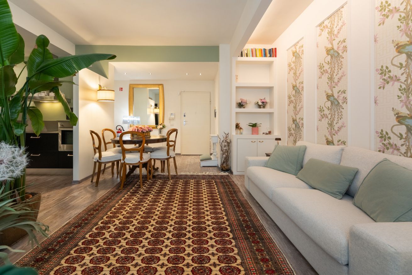 Un salon comprenant un canapé, une table à manger avec des chaises, un tapis à motifs et une bibliothèque agrémentée d’objets décoratifs.