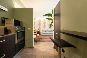Eine kompakte Küche mit modernen Geräten, ein Essbereich mit einer Couch und Stühlen sowie eine große Pflanze.