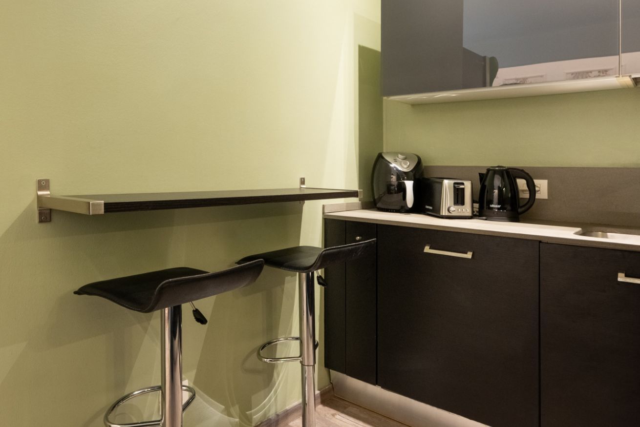 A kitchen with two bar stools, a coffee maker, a toaster, and a kettle on the counter.