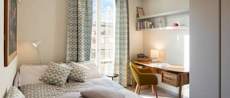 A bedroom with a bed, a desk, a chair, a lamp, and a window with curtains.