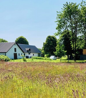 A white building with a sloped roof, surrounded by a field and trees.