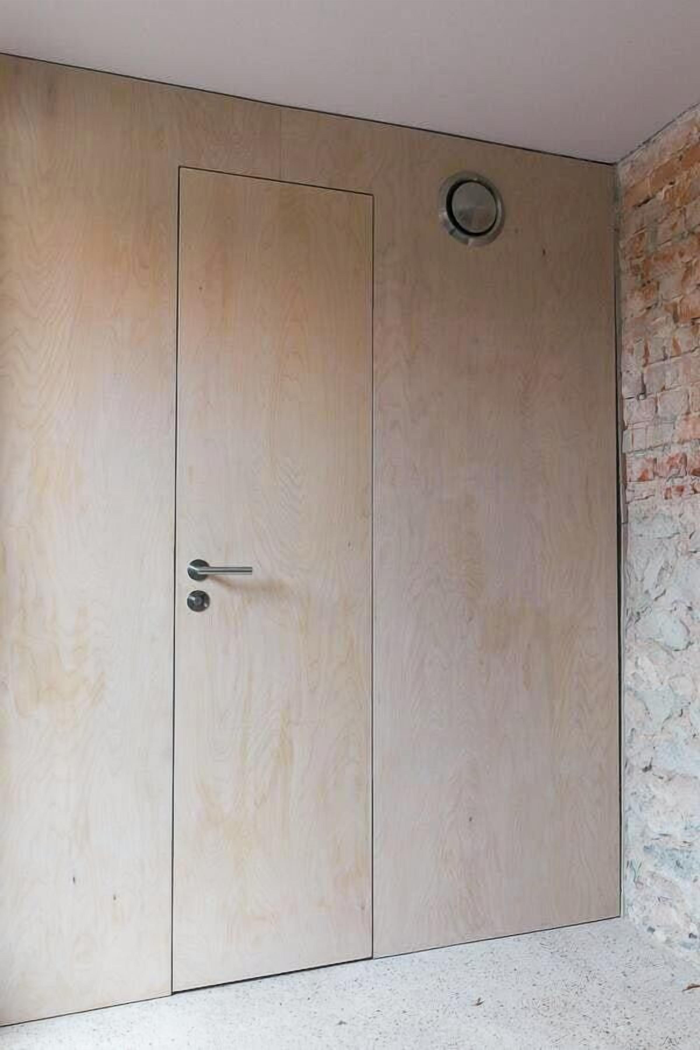 A wooden wardrobe with a door and a small circular vent on the wall.