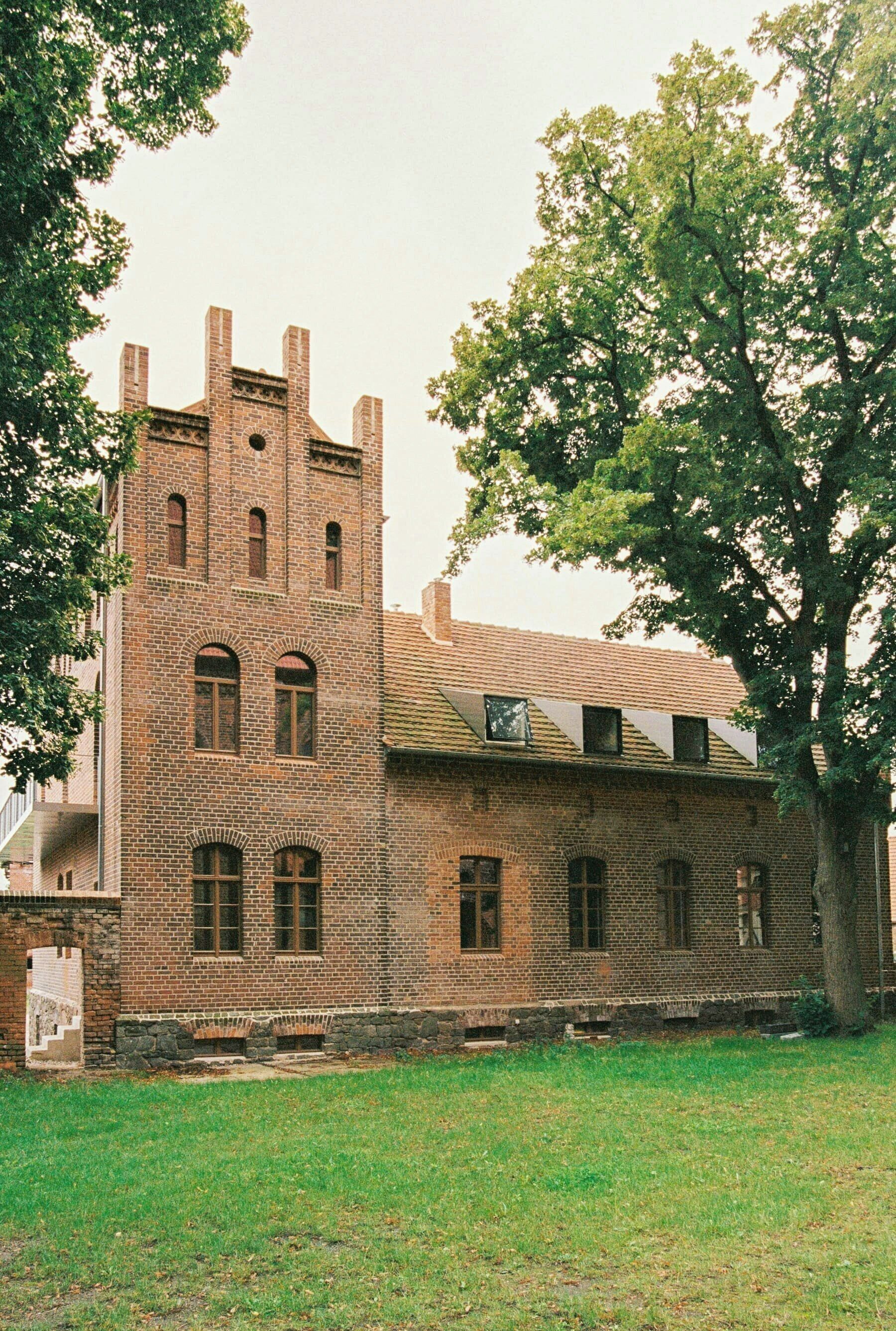 Un edificio histórico de ladrillo con una torre, ventanas amplias y un área verde delantera.
