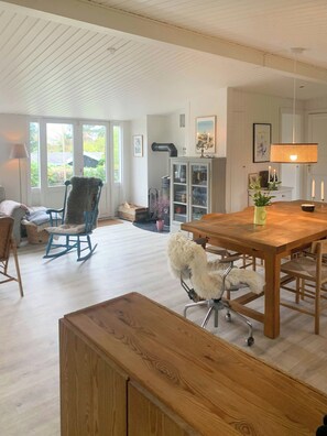 Amplia habitación con una mesa de comedor de madera, una mecedora, una silla para mascotas y un banco.