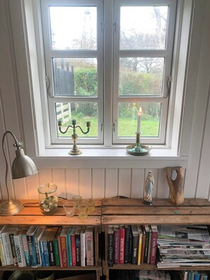 Una habitación con ventana, un candelabro, una estatua y una estantería llena de libros.