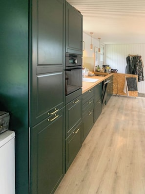 A kitchen with dark cabinetry, a wooden countertop, and a hanging coat rack.