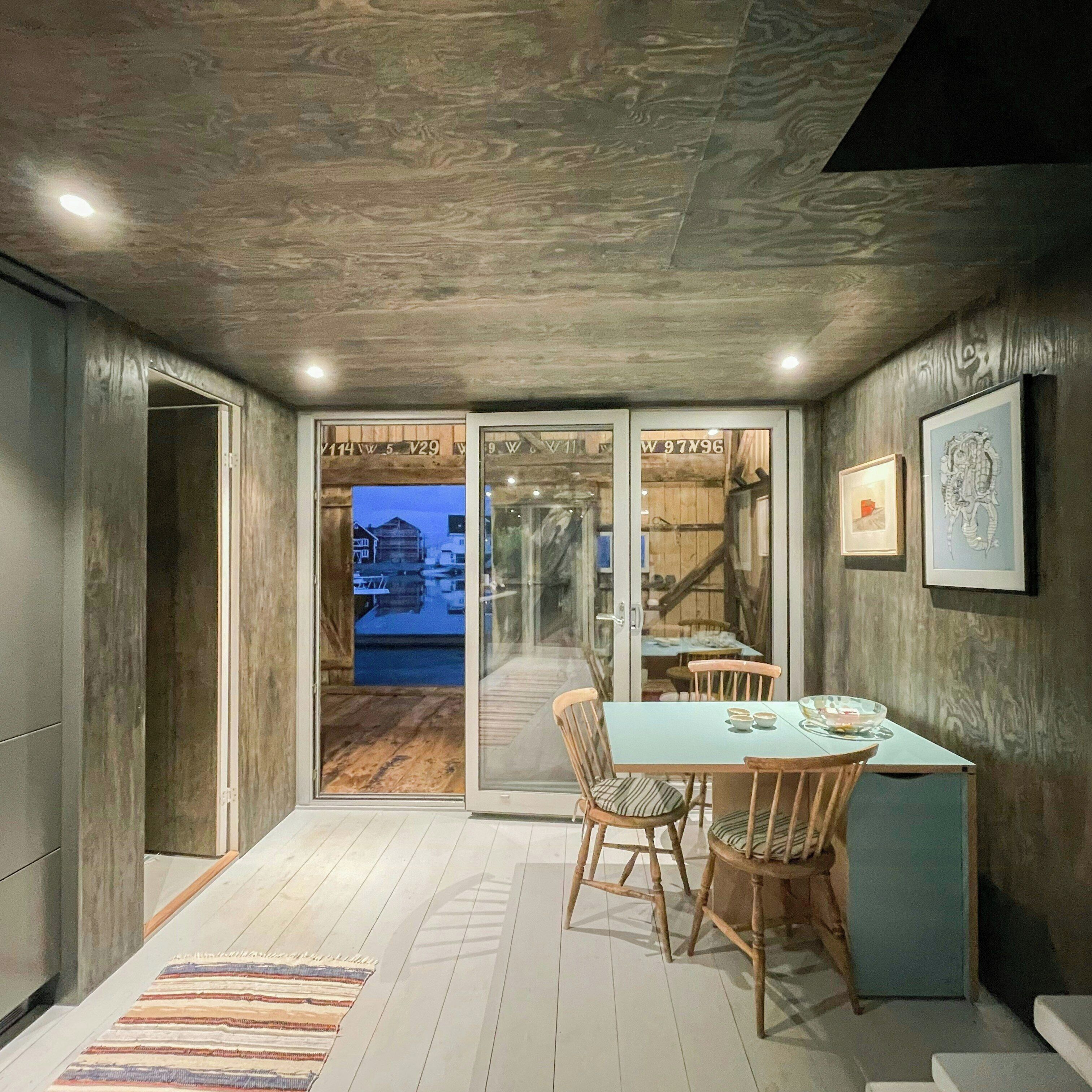 A dining area with a table and chairs, a view through glass doors to an outdoor area, and framed artwork on the wall.