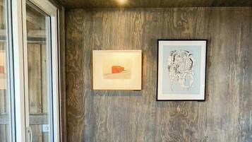 Ein Essbereich mit Glastür, zwei Stühlen, einem Tisch und zwei gerahmten Kunstwerken an der Wand.