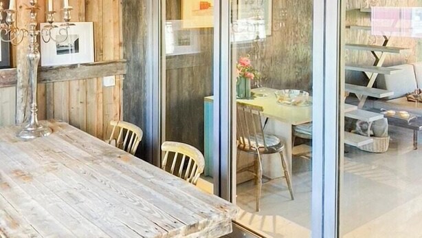 A rustic wooden interior with a dining table, chairs, and a glass partition.