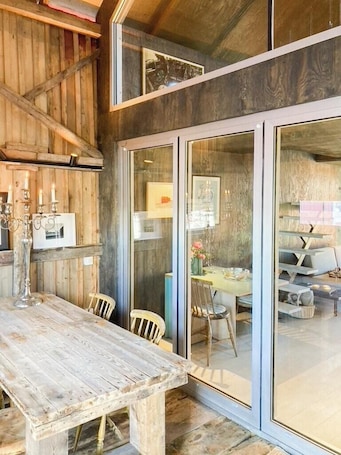 A rustic wooden interior with a dining table, chairs, and a glass partition.